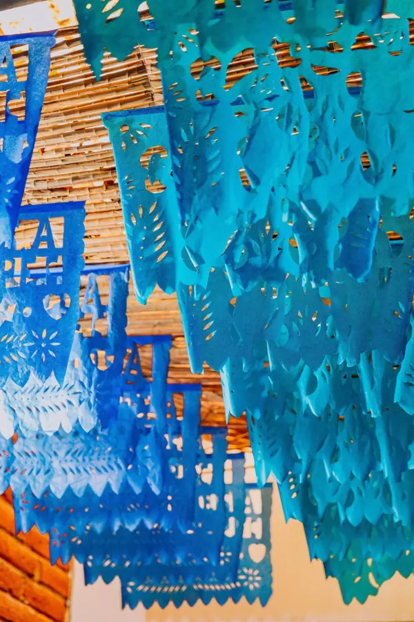 Papel picado azul colgando bajo un techo de carrizo